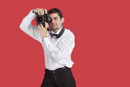 混合种族男子在红色背景上用数码相机拍摄照片高清图片