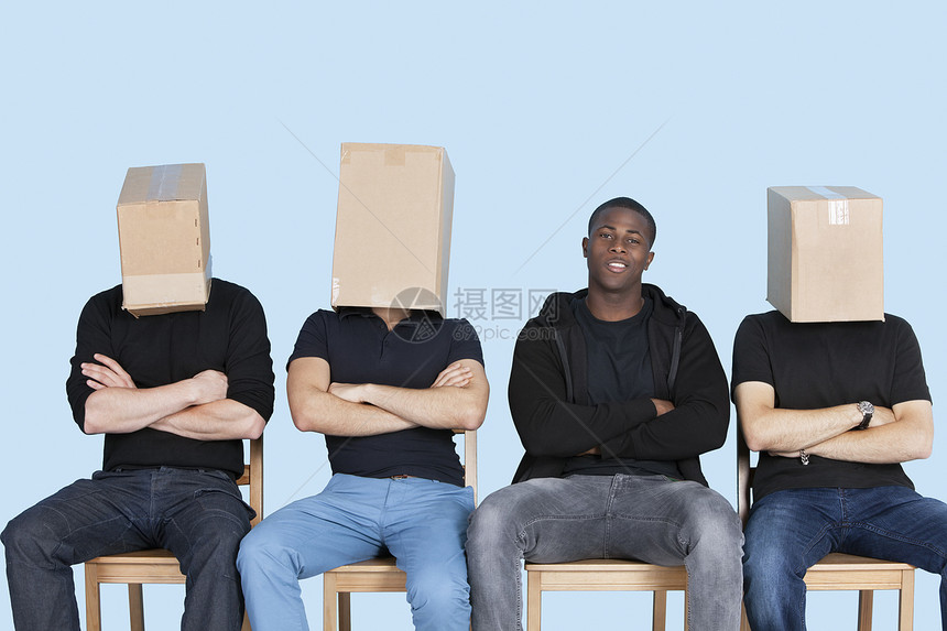 有朋友面相的男人 在蓝背景的椅子上坐椅时被纸板盒遮盖着图片