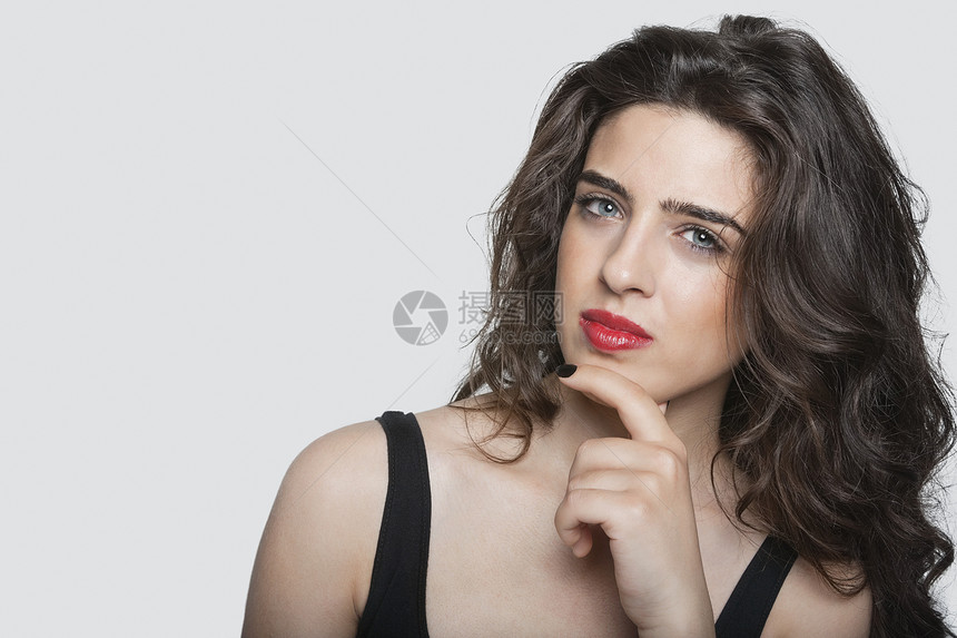 一个深思熟虑的年轻女人的肖像 手在下巴上的灰色背景图片