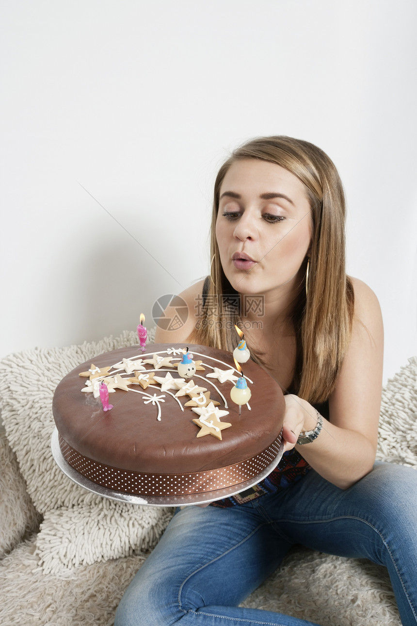 年轻女人在生日蛋糕上吹蜡烛图片