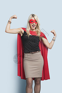 穿着彩色超级英雄穿着超级英雄服装的兴奋的年轻金发美女肖像 穿着轻蓝背景的柔臂背景
