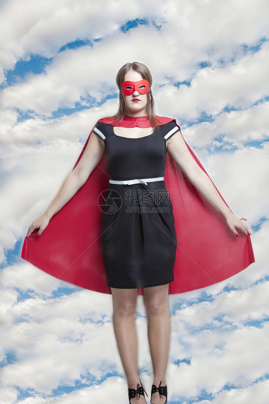 穿着超级英雄服装的年轻女子面对阴云的天空的肖像图片