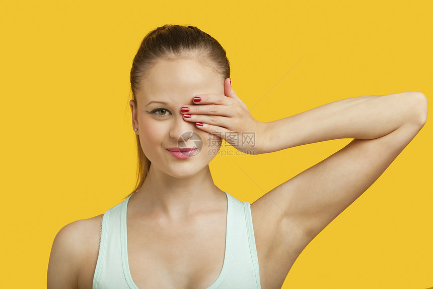 一个美丽的年轻女人的肖像 蒙着黄色背景的双眼女性影棚幸福手指成年背心彩色双手头肩眼睛图片