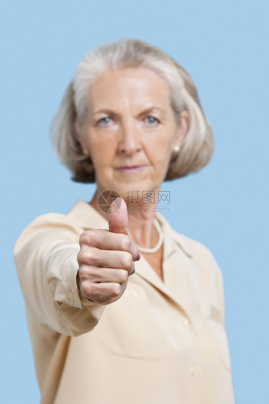 在蓝色背景下伸缩拇指的休闲妇女中 高级妇女的肖像图片