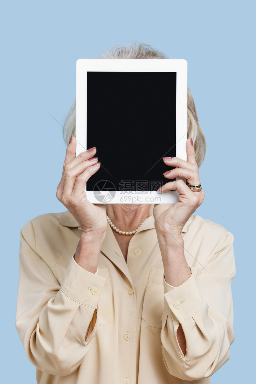 高级女性在蓝色背景下将平板电脑放在脸前的表情图片