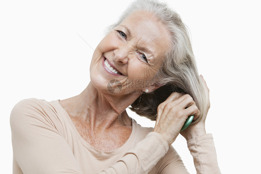 微笑着的老女人在白色背景下梳理头发的肖像图片