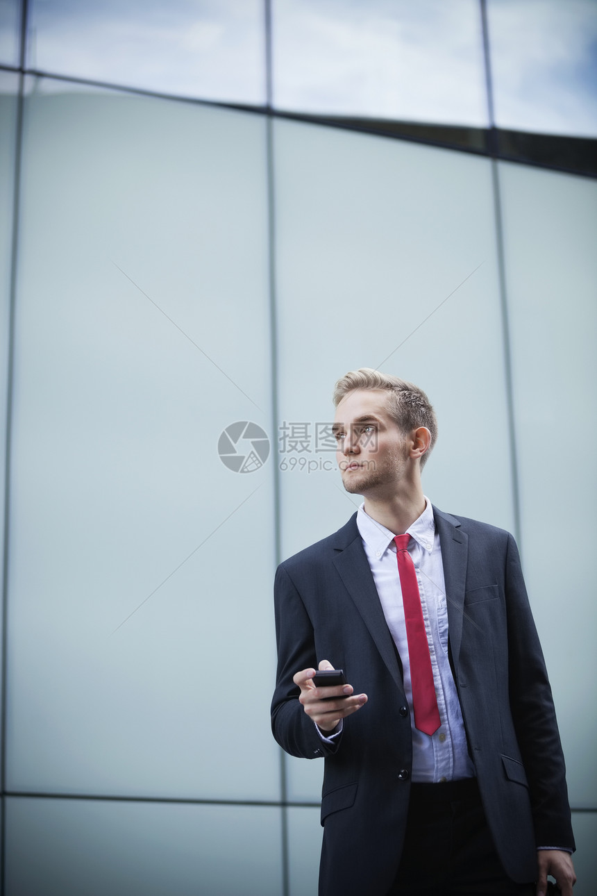 年青商务人士 手机站在玻璃楼对面的青年商务人士图片