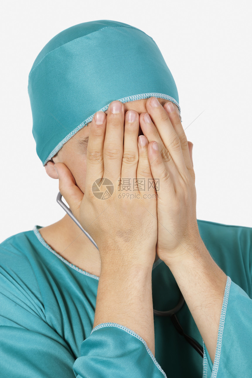 一位心烦意乱的男性外科医生 用灰色的背景用双手遮面图片