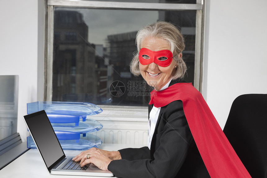 在办公桌使用笔记本电脑制作超级英雄服装高级女商务人士肖像图片