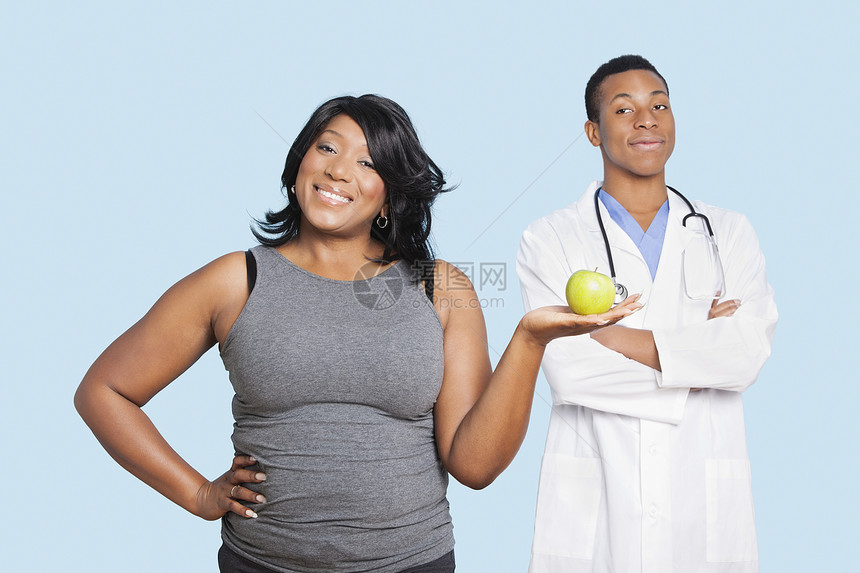 超重混血种族妇女持有绿色苹果 蓝色背景医生兼医生;图片