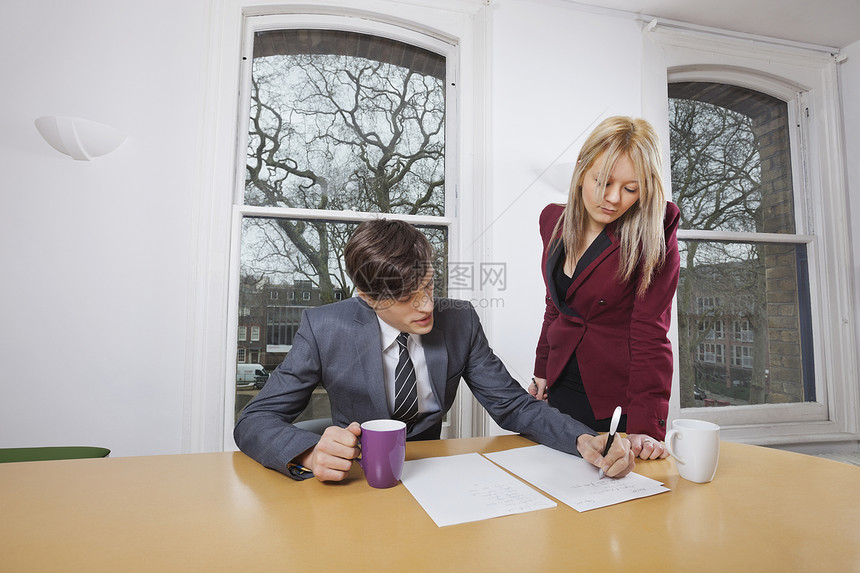 青年商业女青年 在会议桌上看男同事在文件上签名图片