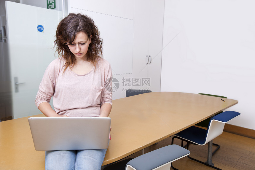 坐在桌上从事笔记本电脑工作的年轻妇女图片