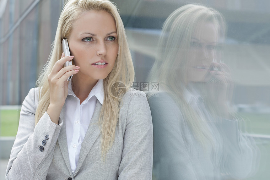 美丽的年轻女商务人士在用手机交谈时 望着玻璃墙而去图片