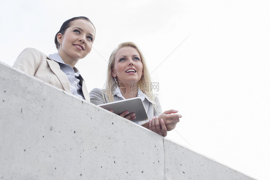 年轻女商务人士的低角度视角 她们以数字平板电脑向远看而站在天边的露台上图片