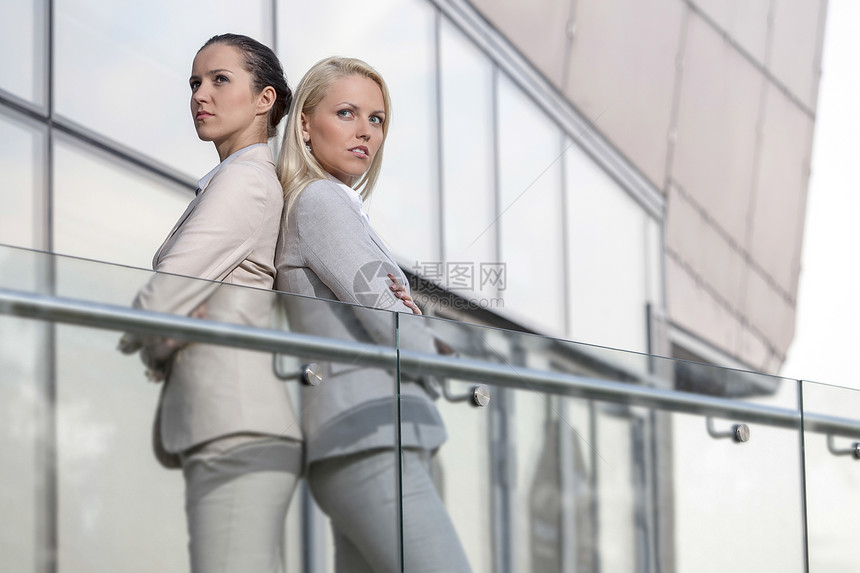 严肃的年轻女商务人士在办公室栏杆上背靠背站着阳台业务高管女性办公楼愤怒建筑学员工建筑同事图片