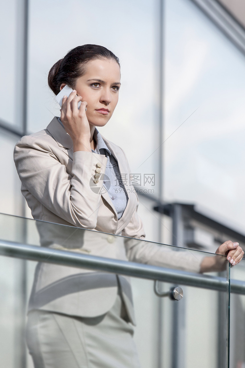 严重的年轻女商务人士在办公室栏杆上使用智能电话通讯员工职业办公楼阳台技术业务玻璃建筑学女性图片
