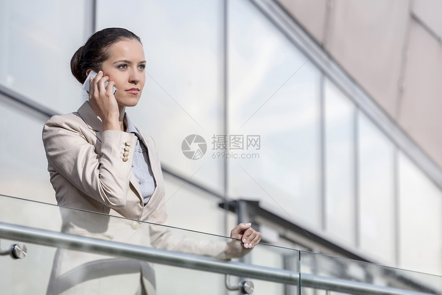 自信的年轻女商务人士 在办公室栏杆上使用智能电话图片