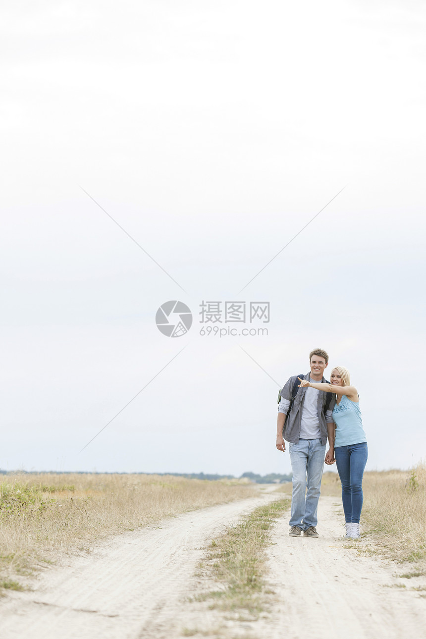 年轻女性徒步旅行者站在田野的足迹上向男子展示一些东西图片
