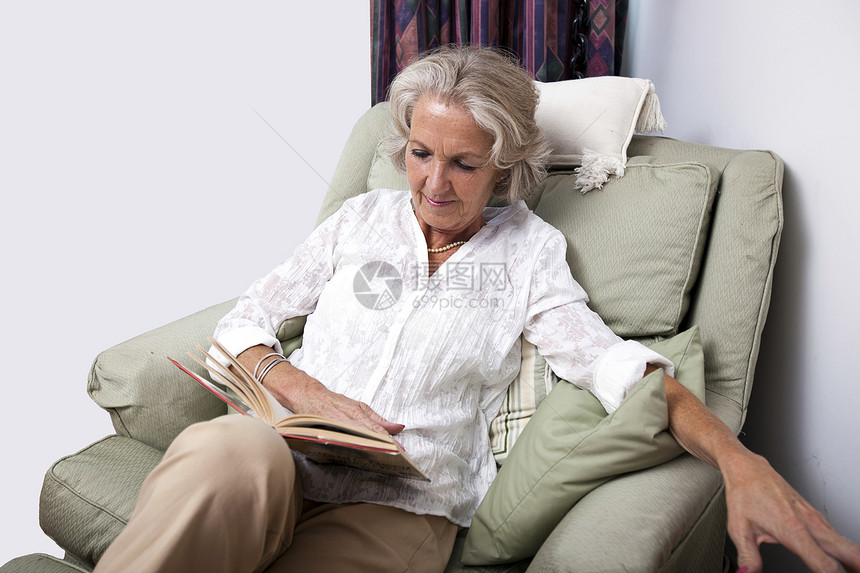 年长妇女在家里放松坐扶手椅时阅读书图片
