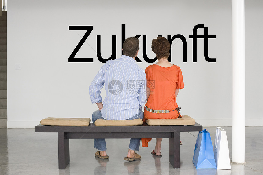 一对坐在长椅上的一对夫妇的后视线 在墙上读德文“Zukunft”(未来)图片
