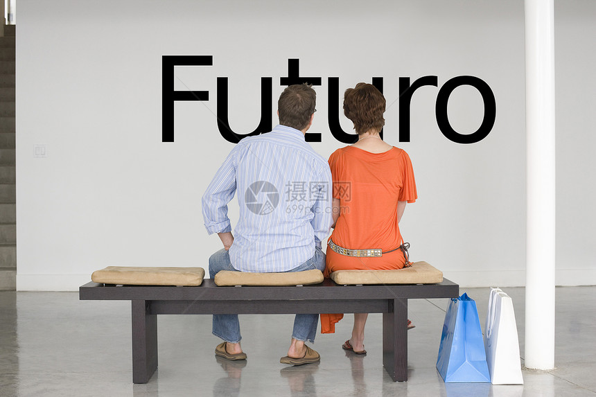 坐在长椅上的一对夫妇的后视线 在墙上读西班牙语文本“Futoro”(未来)图片