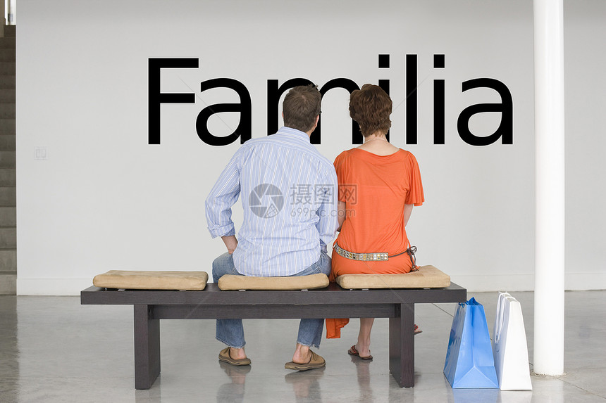 坐在长椅上的一对夫妇的后视线 在墙上读西班牙语文本“Familia”(家庭)图片