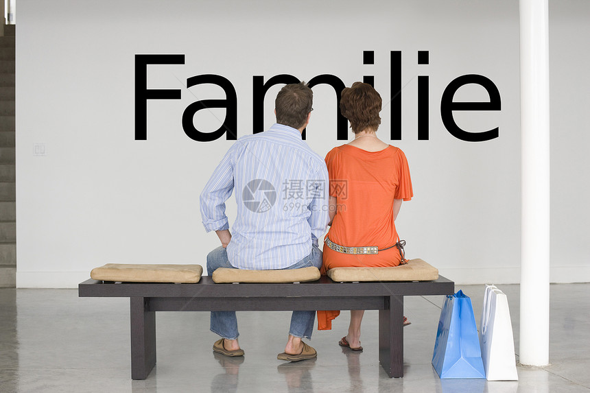 坐在长椅上的一对夫妇的后视线 在墙上读德文“Familie”(家庭)图片