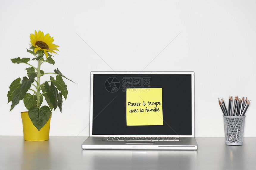 桌上的向日葵植物和便签纸 笔记本电脑屏幕上写着法语文字“”图片