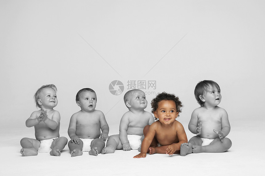 坐在地板上的女婴和其他婴儿一起往远处看图片