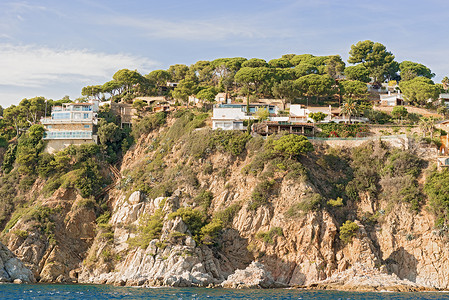 西班牙加泰罗尼亚的旅游房屋蓝色目的地日落悬崖海岸线海滩树木背景图片
