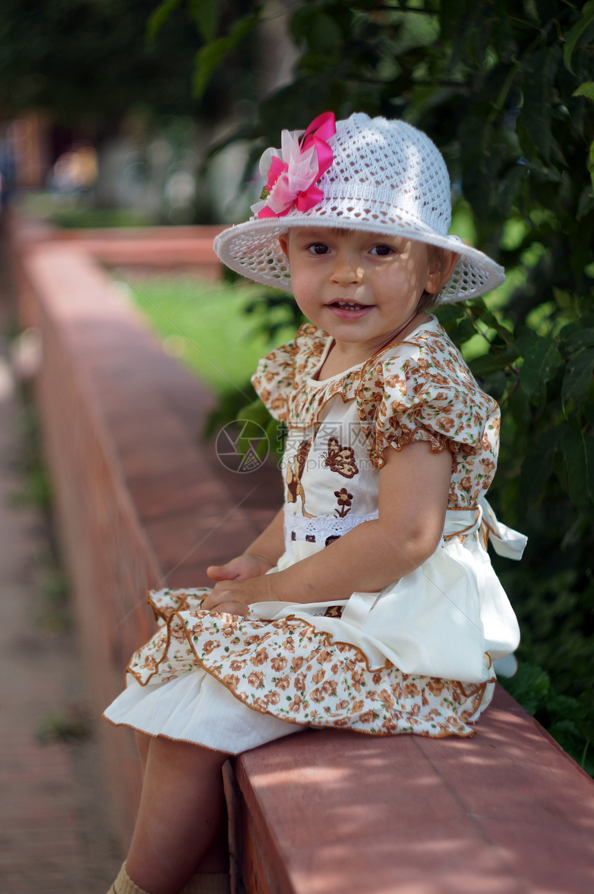 两岁女孩穿着聪明的裙子 戴着帽子坐在街上图片