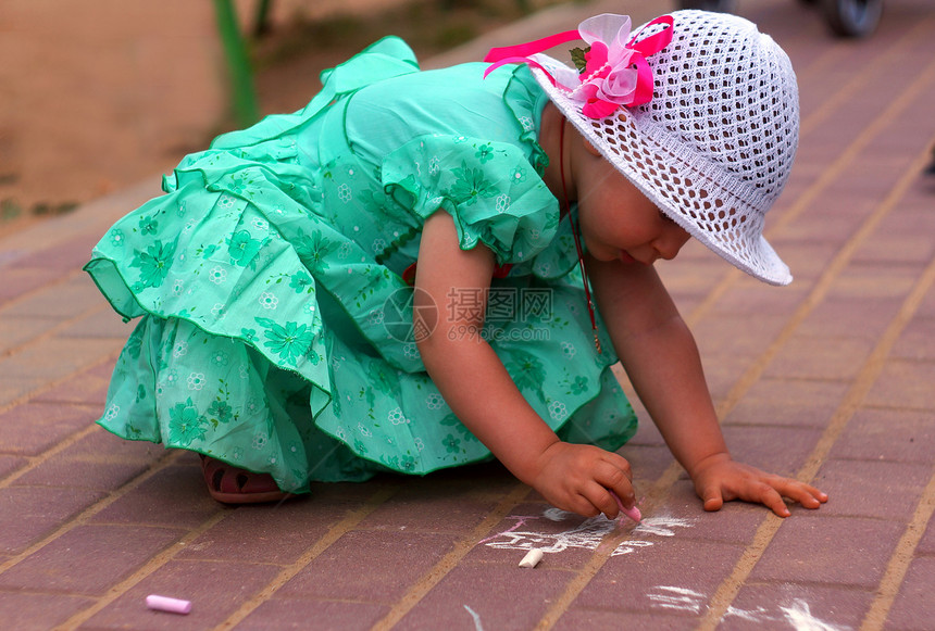 两岁女孩在街上画粉笔创造力绿色游戏帽子连衣裙童年街道绘画婴儿图片