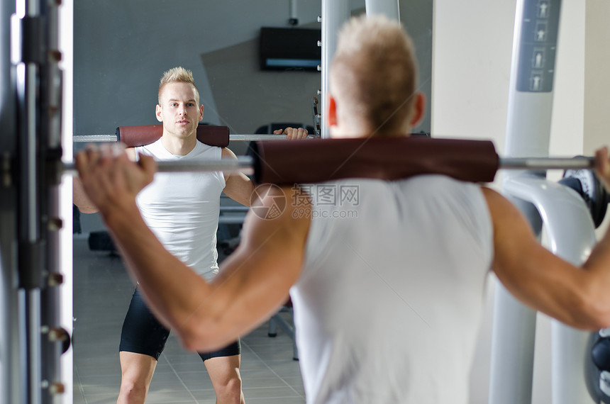 英俊的年轻人在健身房蹲下俱乐部力量肌肉培训师训练下蹲男性成人白色建筑图片