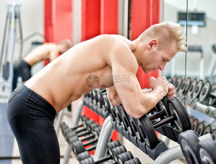 在健身房锻炼后 坐在哑铃机架上休息的年轻人图片