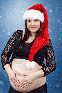 怀着小肚子的漂亮怀孕的圣塔孕妇妈妈生活腹部帽子母性婴儿微笑父母女性育儿背景