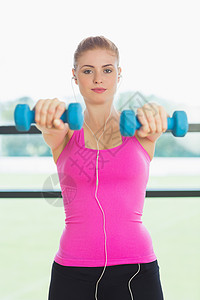 健身工作室中适合运动的女子在健身房用哑铃锻炼女性音乐力量背心重量头发护理调子浅色女士背景图片
