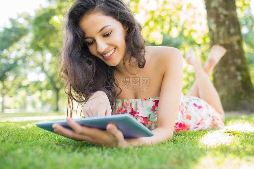 利用平板电脑躺在草坪上的时髦 快乐的黑发美女图片
