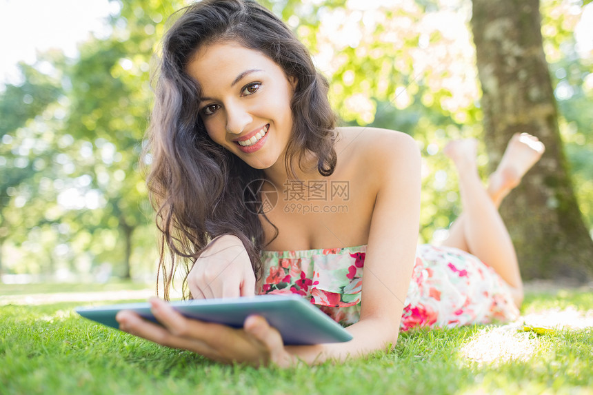 用平板电脑躺在草坪上的 时髦的 笑着脸色的黑发美女图片