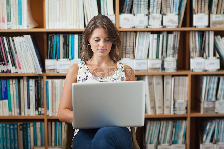女学生在图书馆使用笔记本电脑反对书架知识架子智力书柜图书学校教育互联网专注文学图片