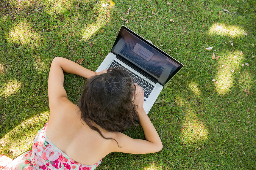 利用笔记本电脑躺在草地上的时尚黑发美女图片