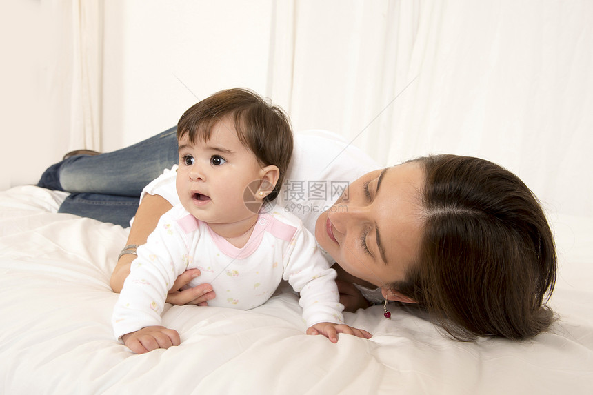 母亲和女儿在与世隔绝的床上玩耍女士牛仔裤妈妈母性拥抱投标幸福微笑女性育儿图片