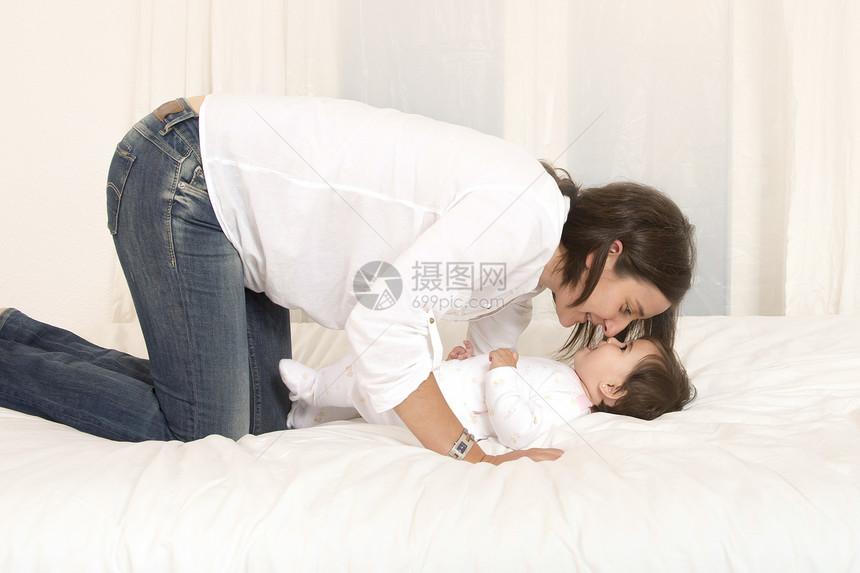 母亲和女儿在与世隔绝的床上玩耍卧室快乐妈妈微笑母性拥抱投标女士头发育儿图片
