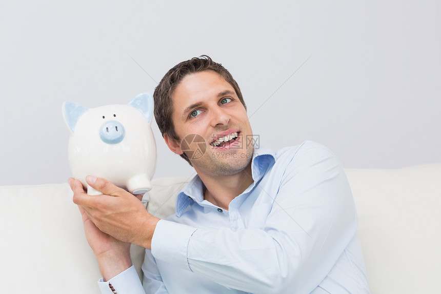 在客厅里有小猪银行的英俊散工蓝色公寓金融房子白色男性存钱罐棕色储蓄衬衫图片