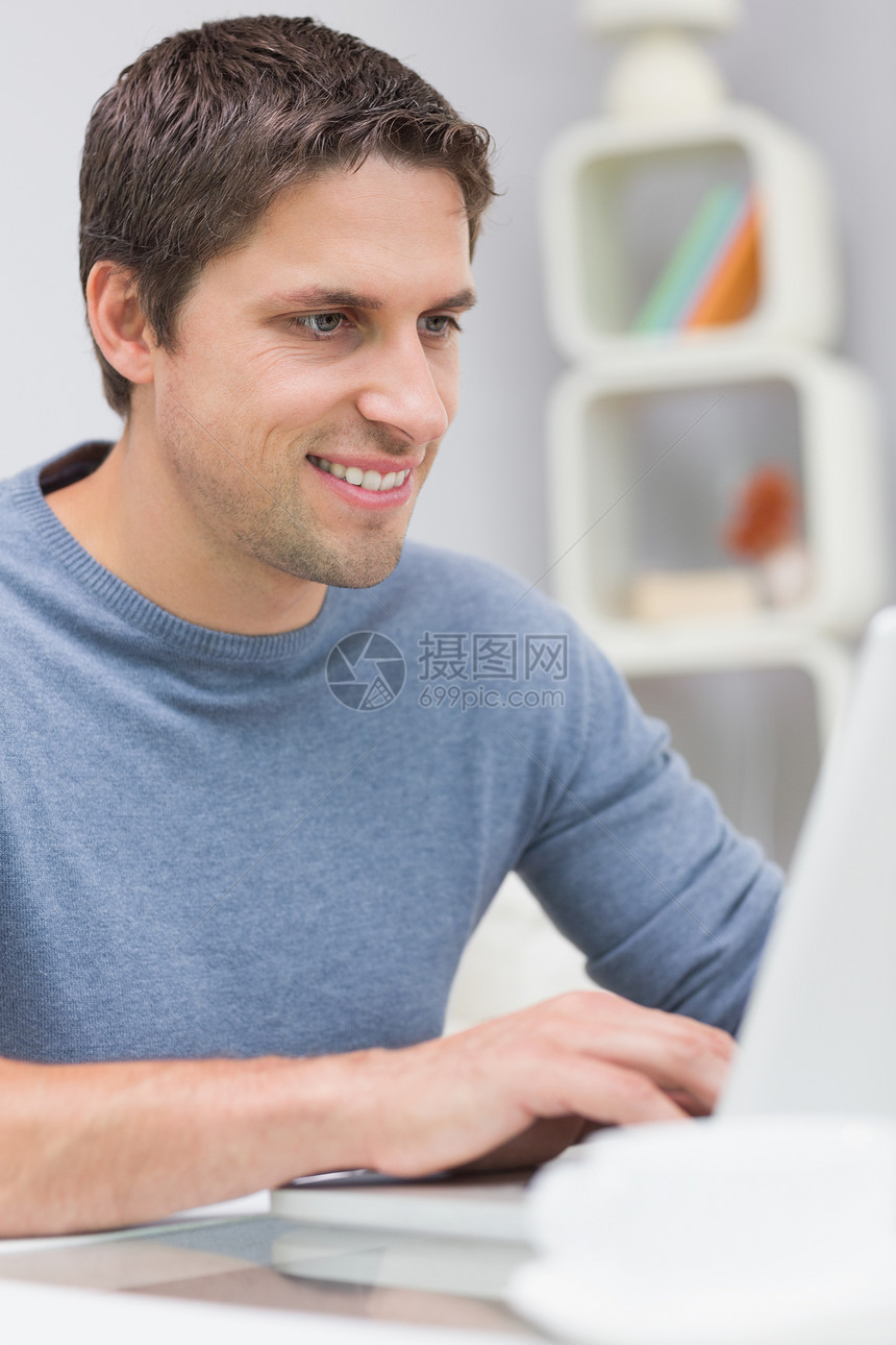在客厅使用笔记本电脑微笑的年轻人技术专注居家办公男人头发男性房子闲暇茶几图片