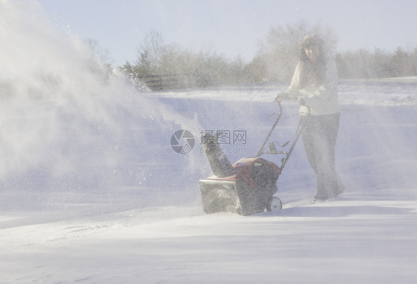 年轻妇女与吹雪者清扫车投掷者季节冷冻车道降雪机器工作打扫女士鼓风机图片