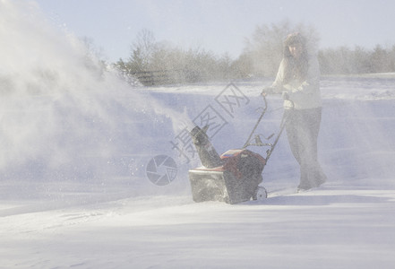 年轻妇女与吹雪者清扫车投掷者季节冷冻车道降雪机器工作打扫女士鼓风机背景图片