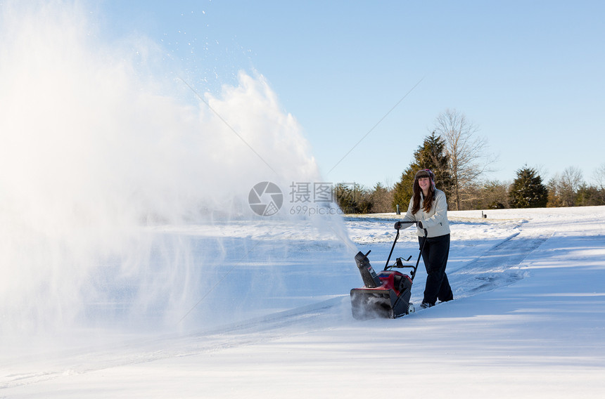 年轻妇女与吹雪者清扫车降雪住宅冷冻天气打扫人行道暴风雪女士机械鼓风机图片