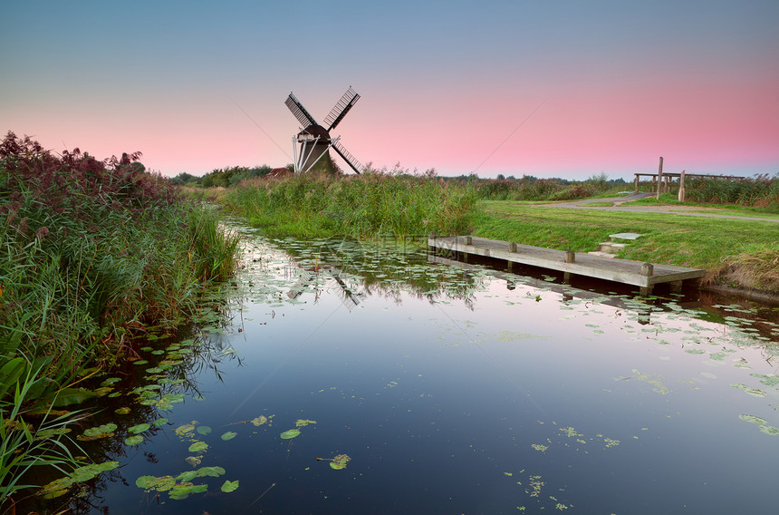 日出时乘河的荷兰风车图片