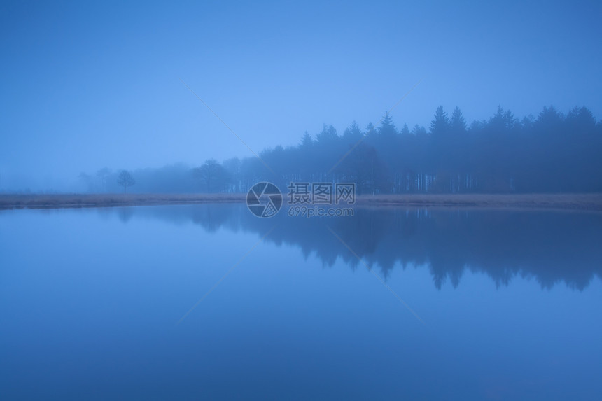 在浓密的黄昏雾中 湖边森林环绕着圆周光图片