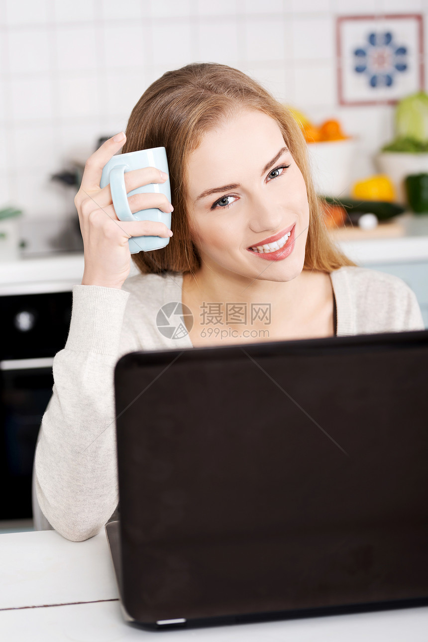 年轻的美女坐在桌子边 用笔记本电脑和杯子房子商业厨房幸福女孩女性咖啡冲浪技术网络图片